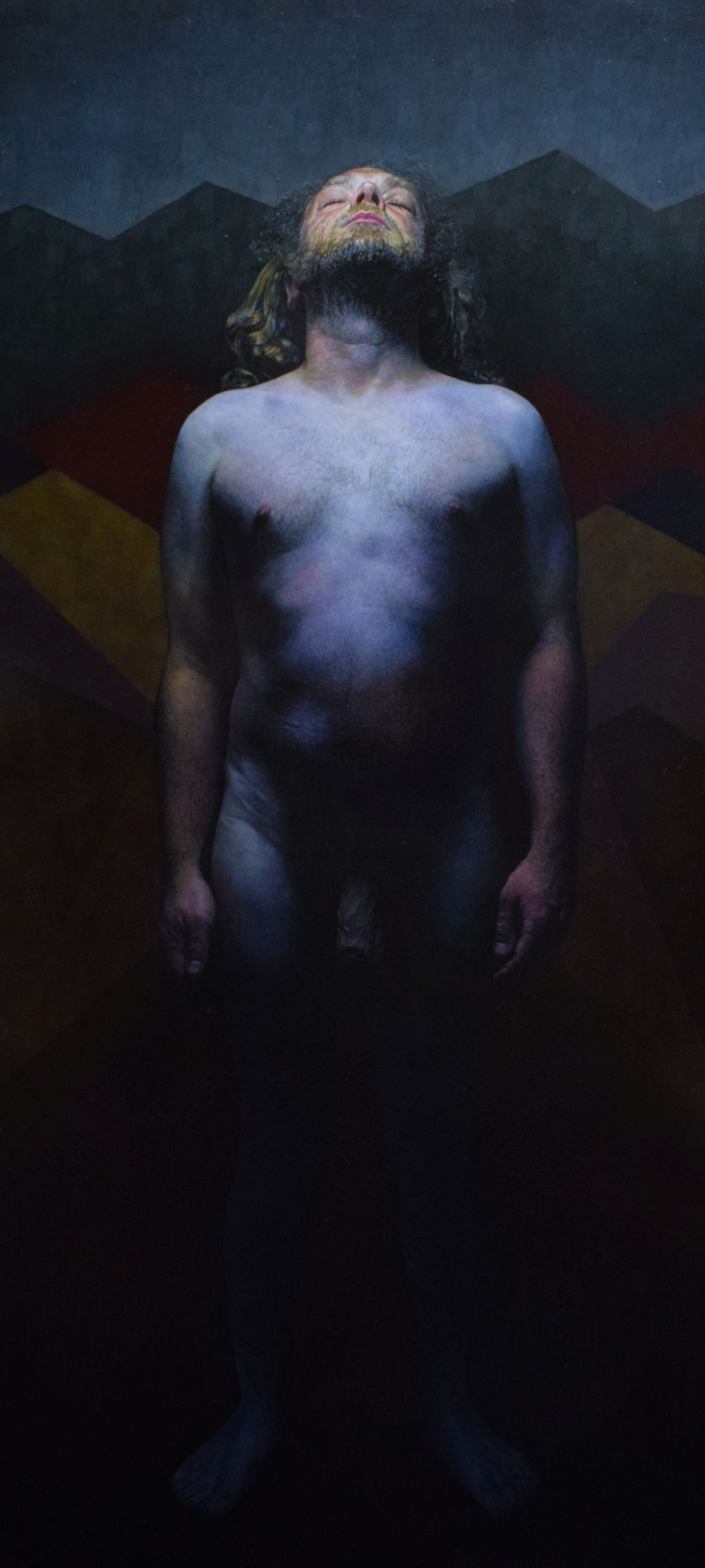 A nude man standing and looking upwards. The light is coming from above.